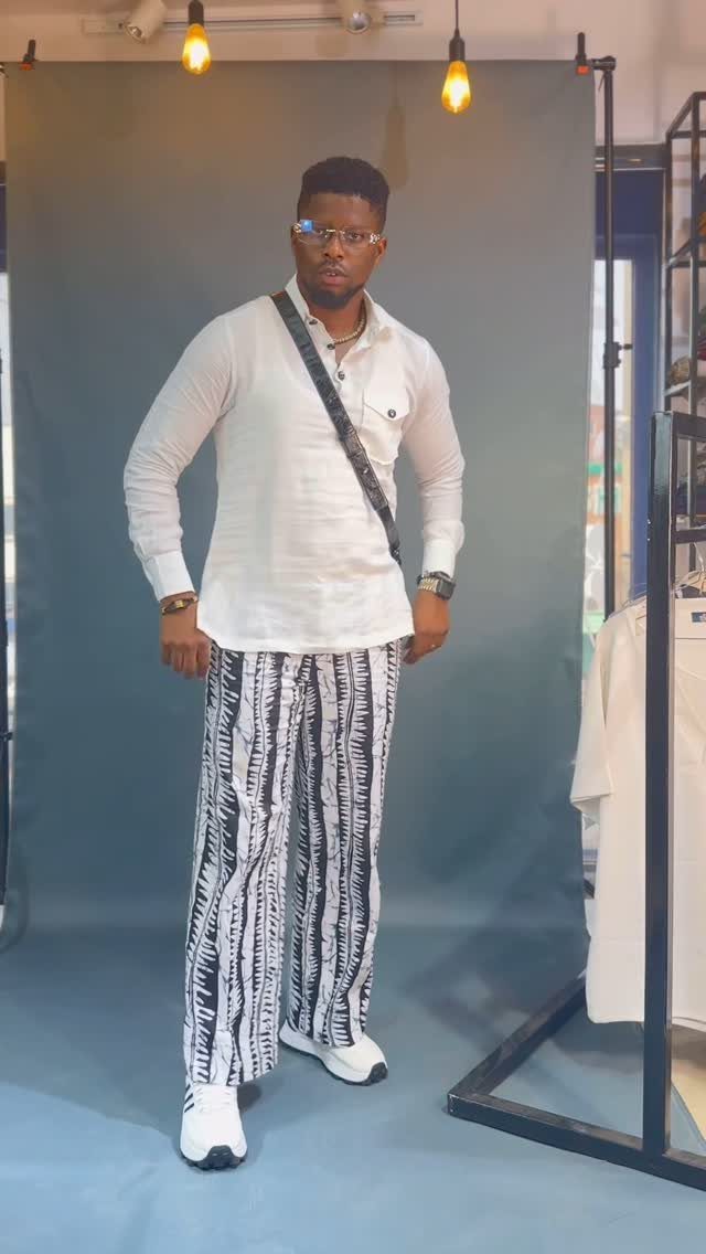 A man wearing a white shirt and black and white printed wide-leg trousers.