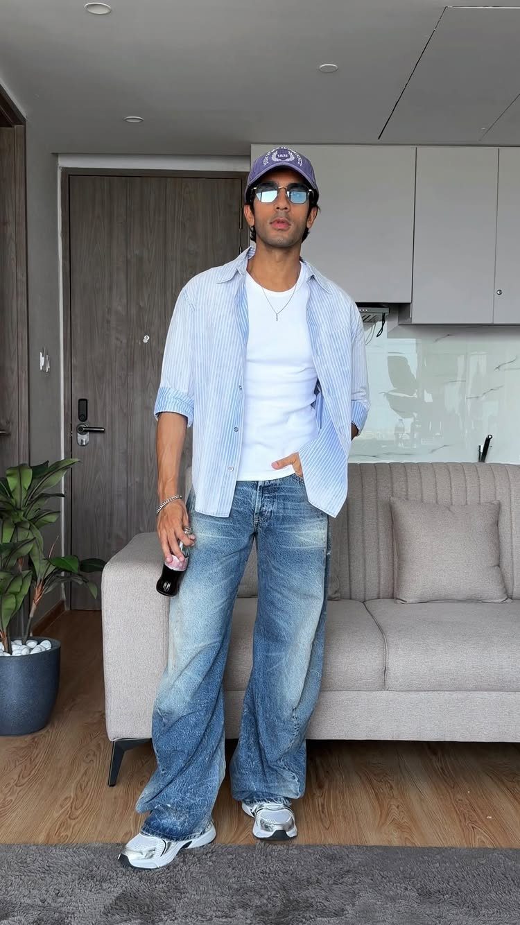 Man in a white tank top, striped shirt, and wide-leg blue jeans standing in a living room.