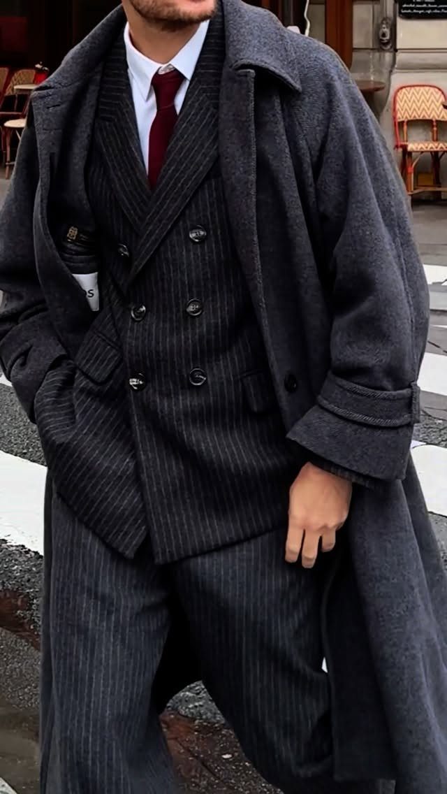 A man wearing a dark pinstripe suit and a heavy charcoal grey wool overcoat.