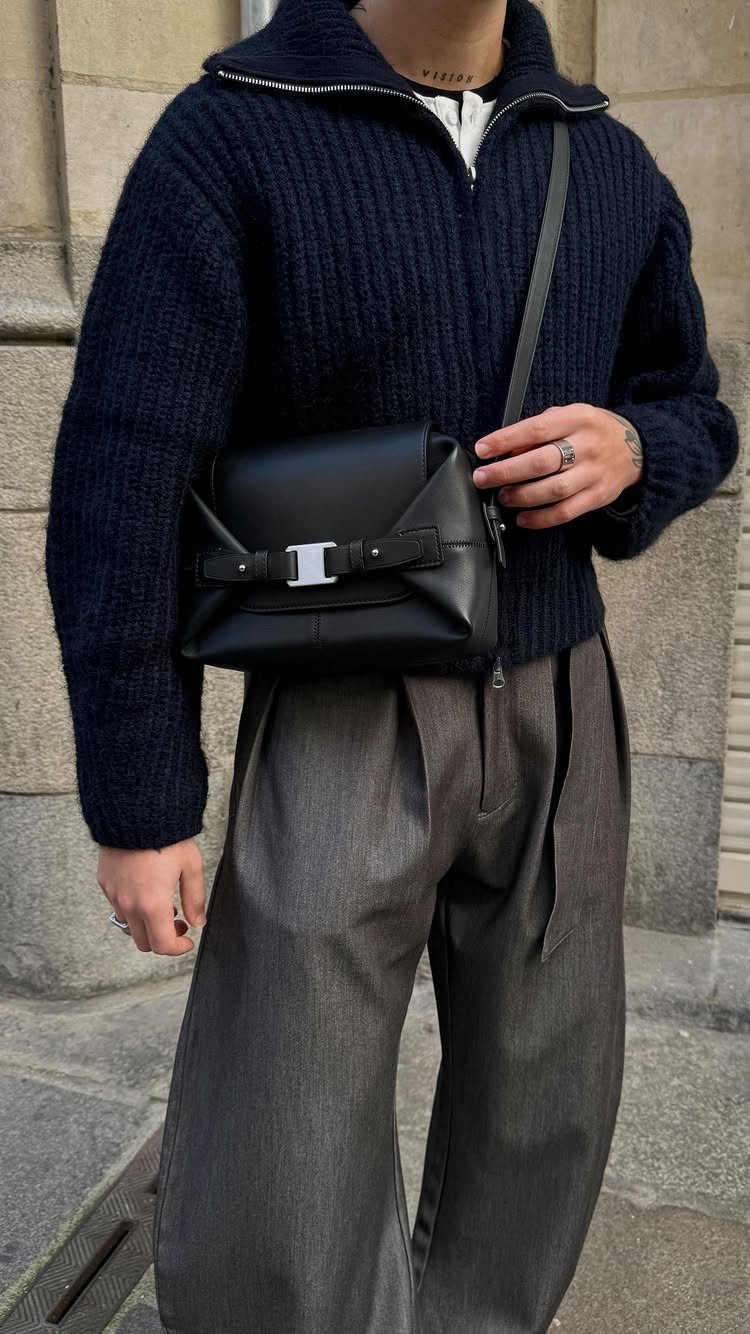 Man wearing a navy ribbed sweater, grey wide-leg trousers, and a black leather crossbody bag.